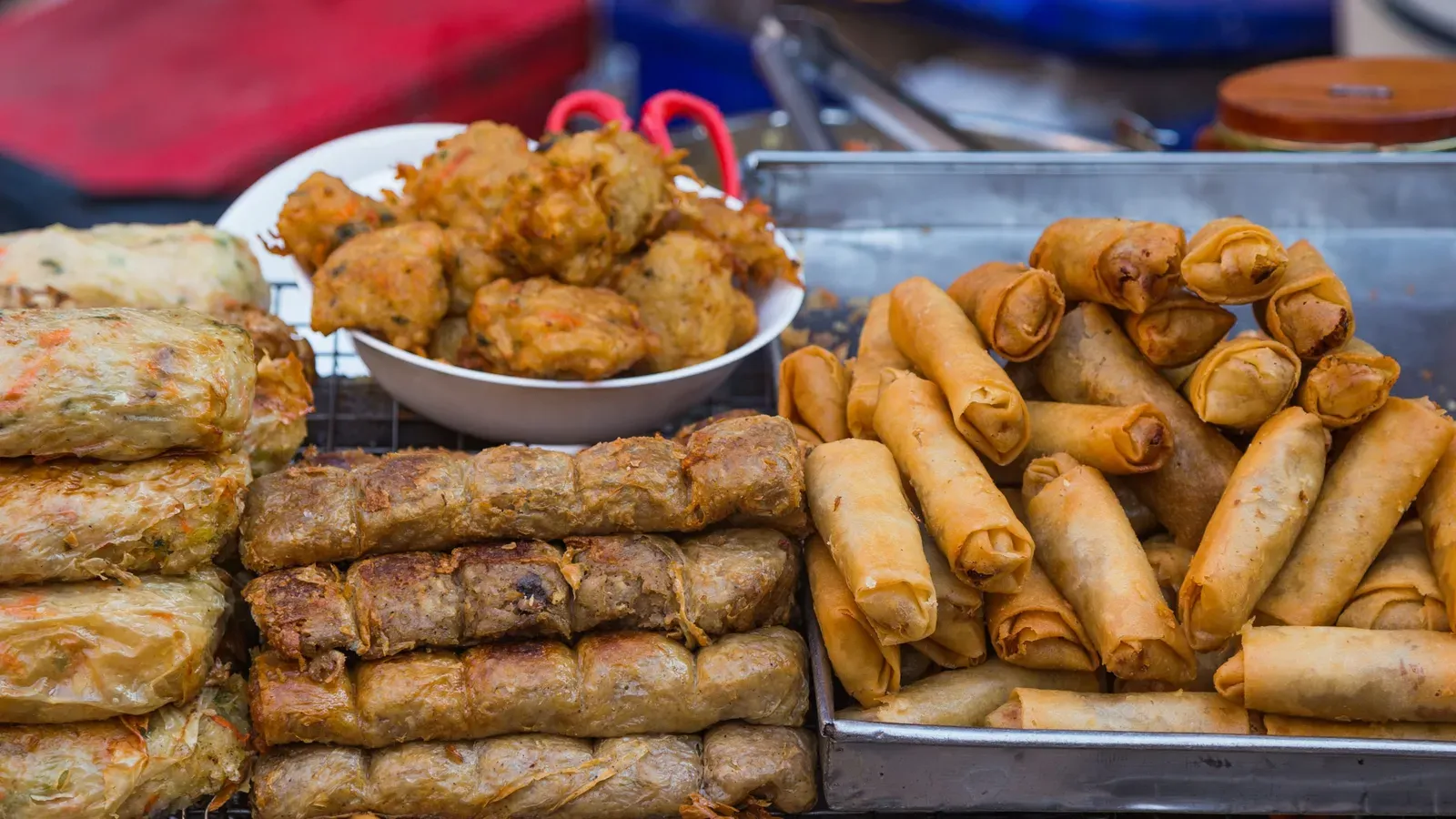 Trays of golden fried spring rolls, stacked deep-fried rolls and a bowl of fritters on a street-food stall