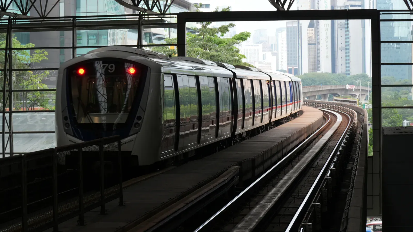A driverless RapidKL Kelana Jaya Line train curving away from the elevated KL Sentral station, with Kuala Lumpur office towers behind