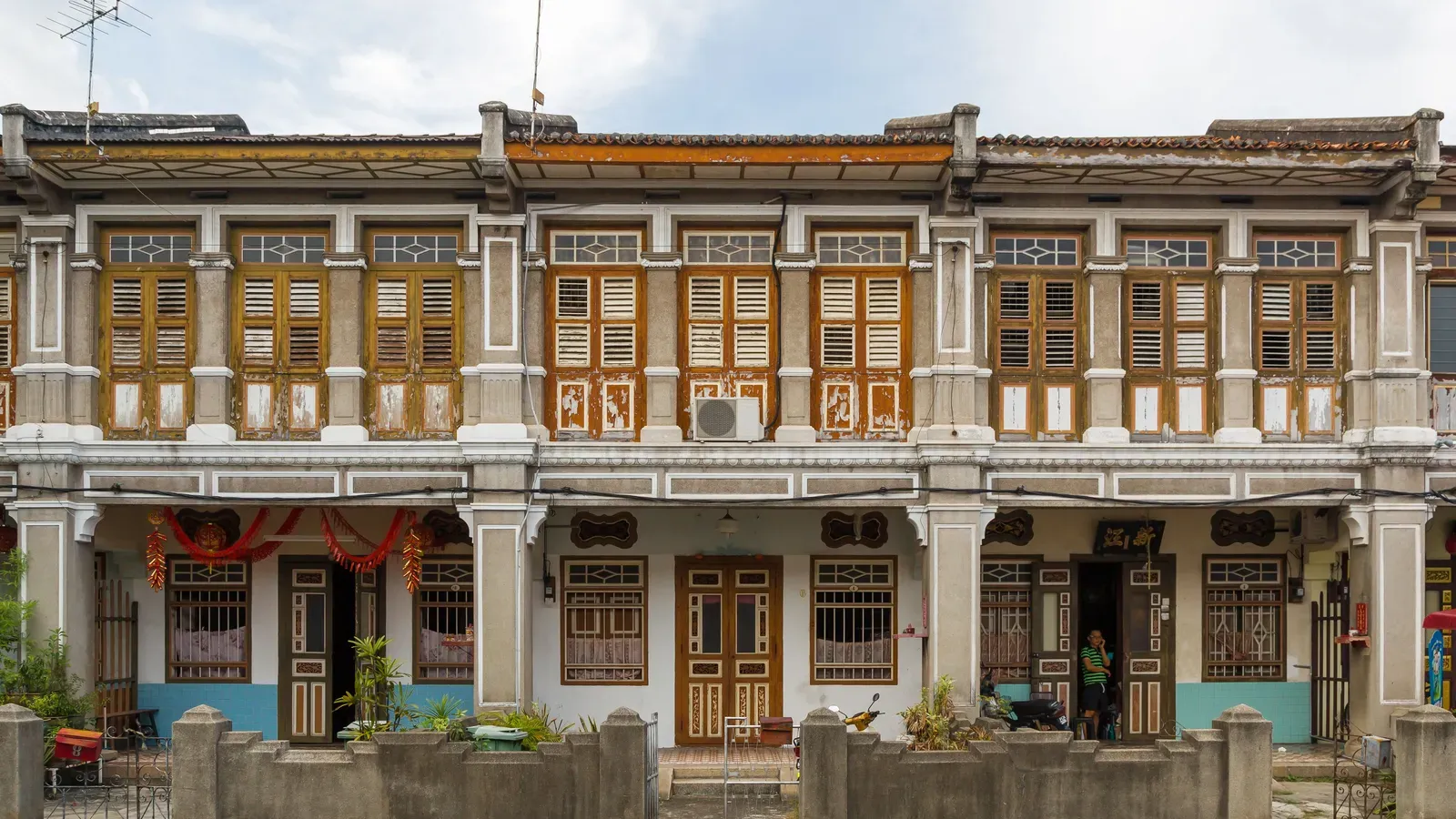 A row of two-storey heritage shophouses with wooden louvred shutters, carved doors and a covered five-foot way behind a low wall