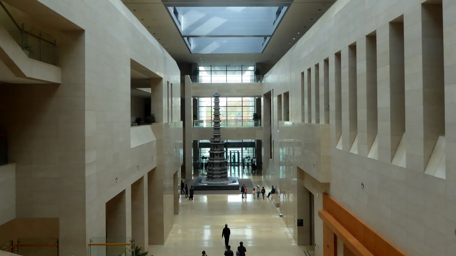 A long, skylit stone hall inside the National Museum of Korea with a tall ten-storey stone pagoda at the far end and a few visitors walking