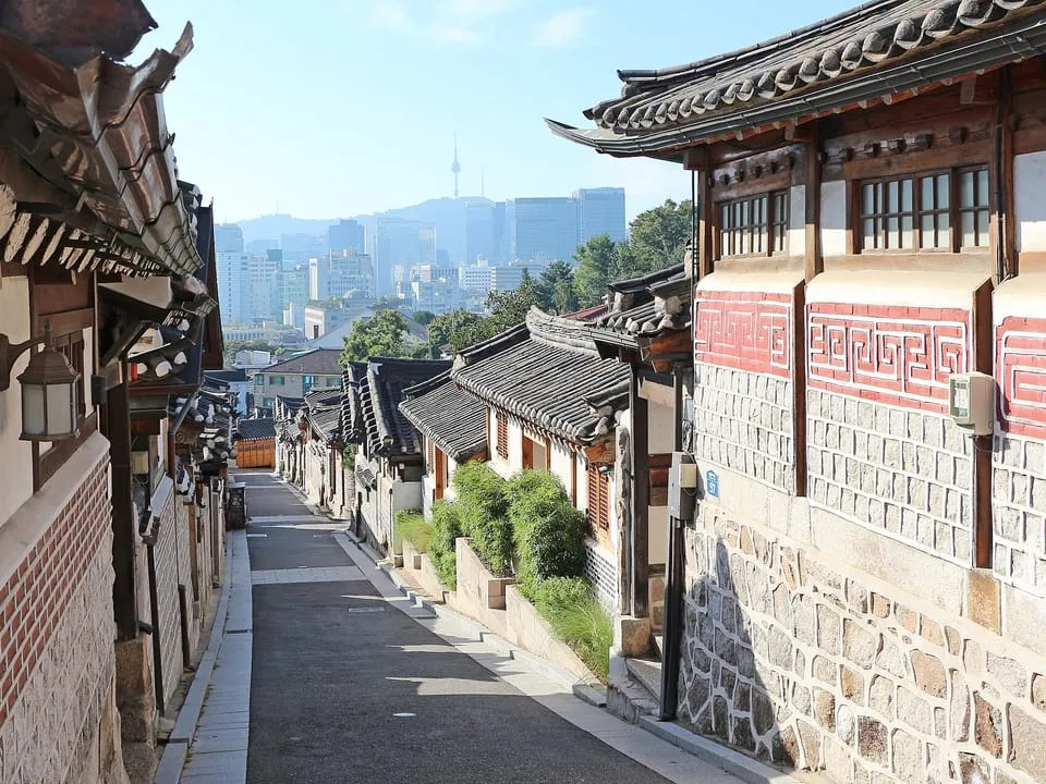 A sloping street of hanok houses in Bukchon Hanok Village, with the city beyond