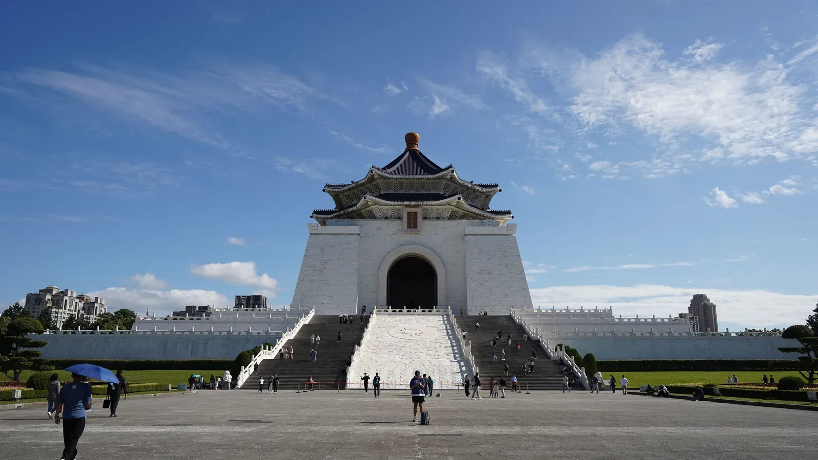 The white Chiang Kai-shek Memorial Hall with its blue octagonal roof at the top of a wide staircase, seen across the paved Liberty Square under a blue sky