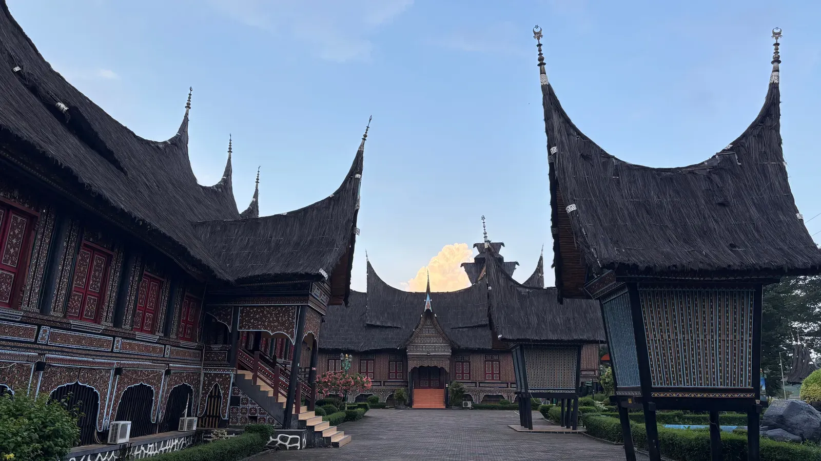 Minangkabau houses and rice barns with tall, curved thatched roofs around a paved courtyard at the West Sumatra Pavilion of Taman Mini Indonesia Indah